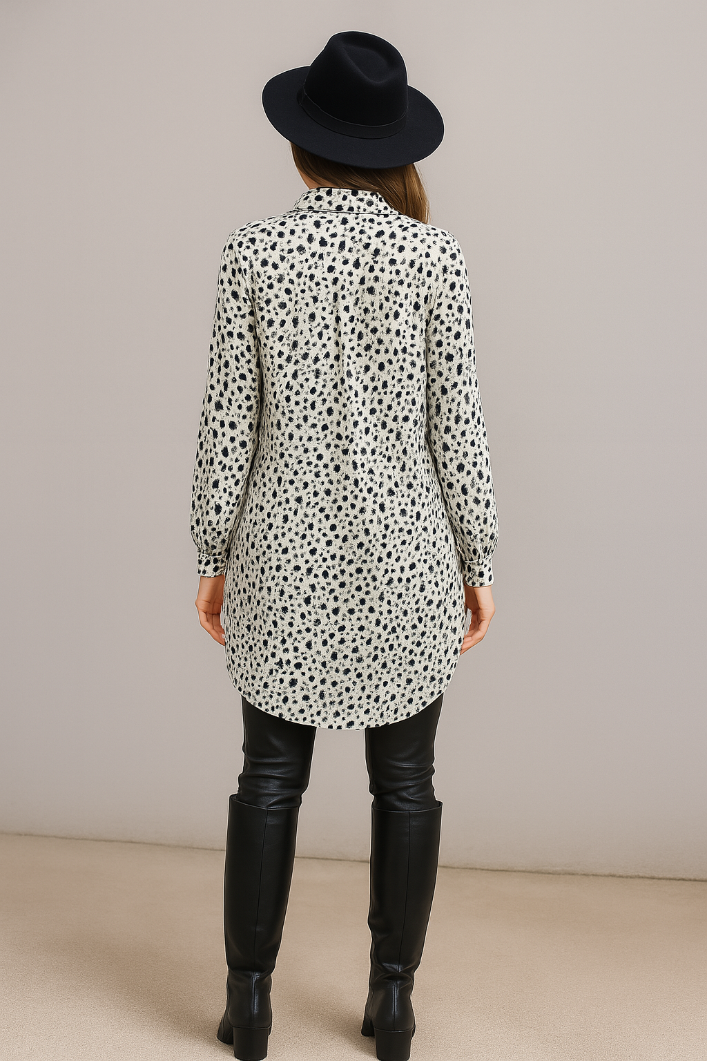 Women wearing a long, patterned shirt with black leather boots and a black hat on a plain background