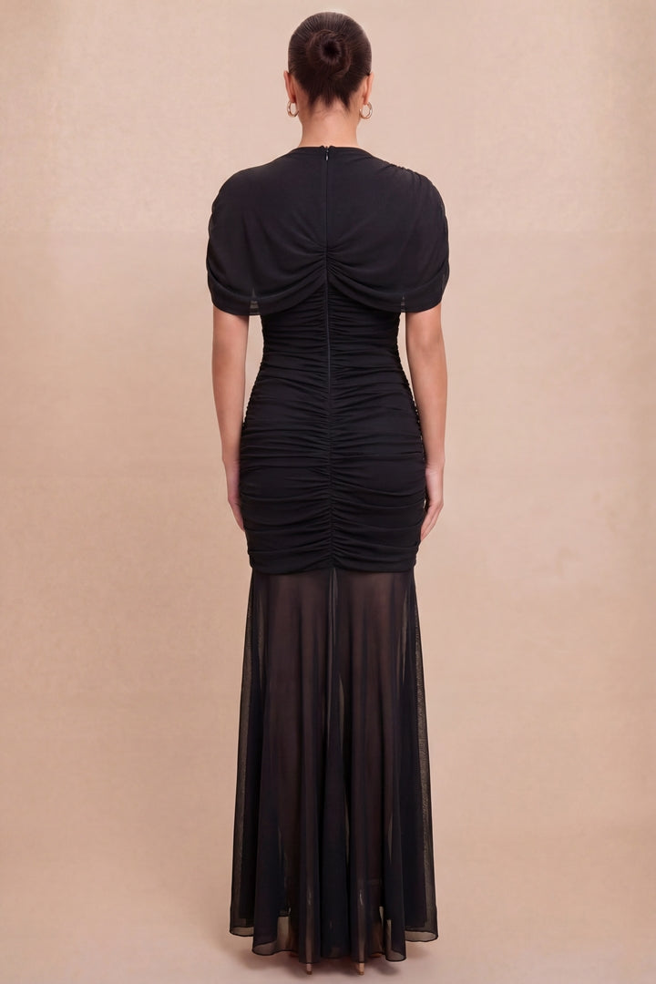 Woman wearing a black dress with sheer overlay on a beige background