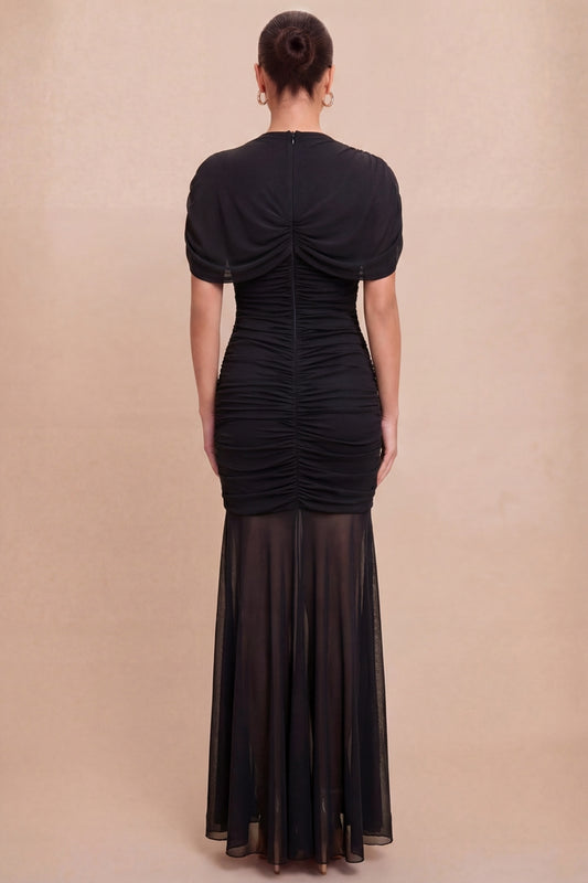 Woman wearing a black dress with sheer overlay on a beige background