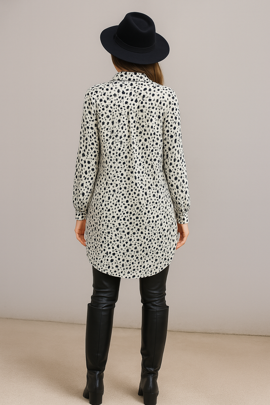 Women wearing a long, patterned shirt with black leather boots and a black hat on a plain background